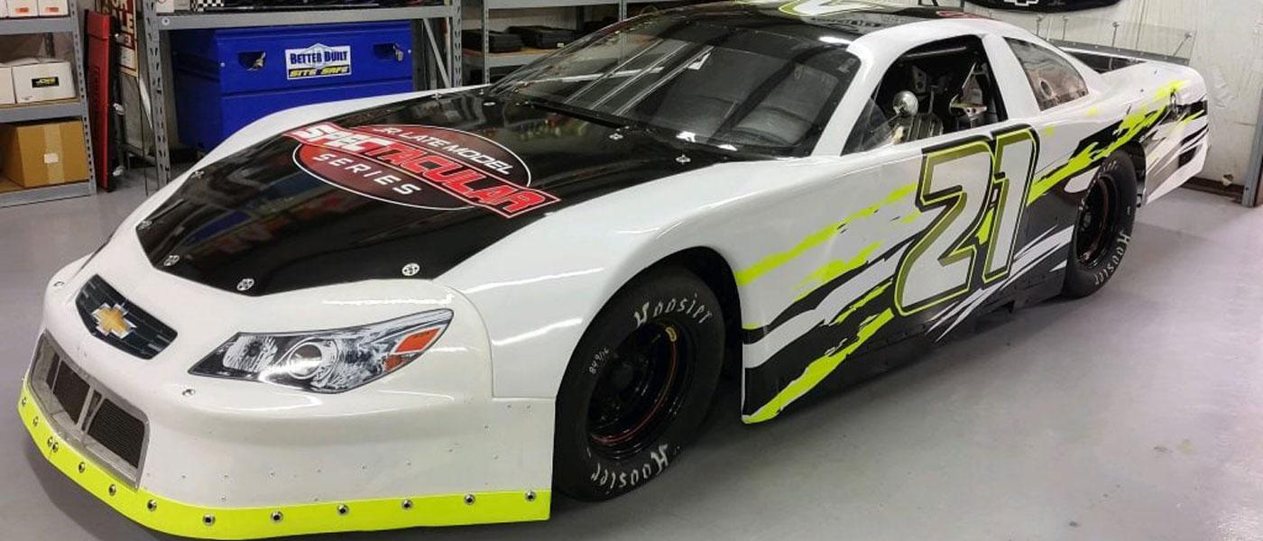 #21 race car with the Jr. Late Model Spectacular Series (JRLMSS) logo on the hood. In a garage setting