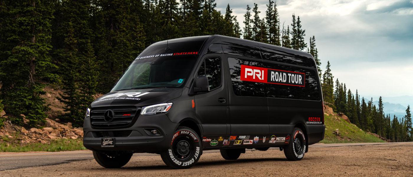 PRI Road Tour van at Pikes Peak with sponsor stickers including AST Suspension Technology, Buzze Racing, Callies Performance Products, Deatschwerks, Design Engineering Inc., Forgeline Motorsports, Hawk Performance, Hot Shot's Secret, KW Automotive, Lucas Oil Products, Marwin Sports, Mass Traction, and RE Suspension