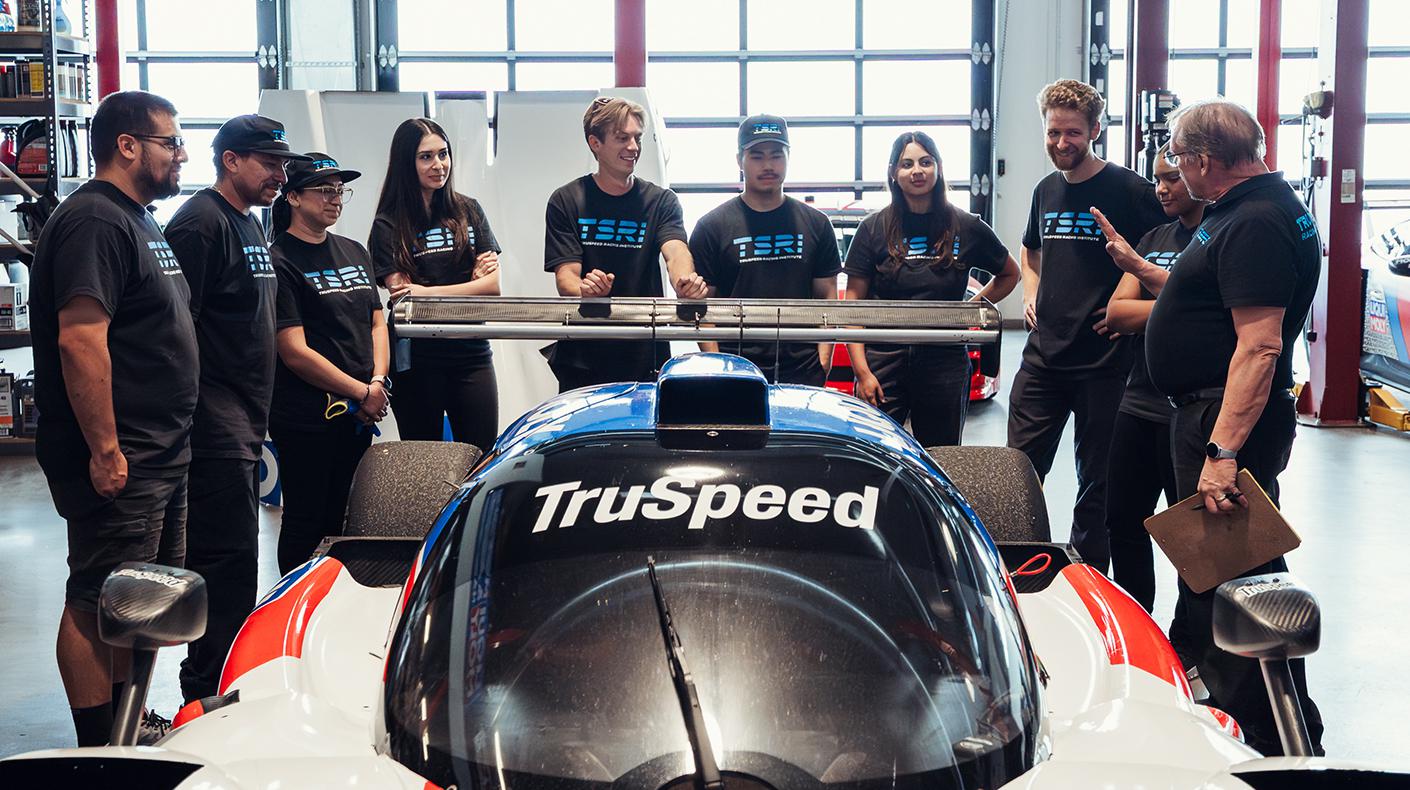 TruSpeed students gathered around a car listening to an instructor. 