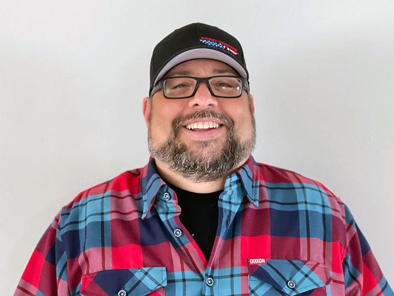 Headshot of Tom Kundrik wearing a hat and flannel shirt