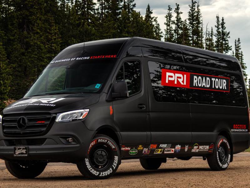 PRI Road Tour van at Pikes Peak with sponsor stickers including AST Suspension Technology, Buzze Racing, Callies Performance Products, Deatschwerks, Design Engineering Inc., Forgeline Motorsports, Hawk Performance, Hot Shot's Secret, KW Automotive, Lucas Oil Products, Marwin Sports, Mass Traction, and RE Suspension