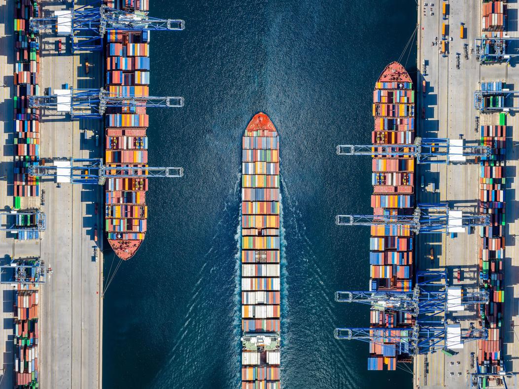Aerial top down view of a large container cargo ship terminal with loading activity and vessel traffic.